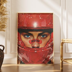 Peut inclure: Impression artistique encadrée représentant un gros plan d'une personne portant un casque de course rouge. La personne a les yeux bleus et un petit autocollant rouge sur le nez avec le mot "Racer". L'œuvre est exposée dans une pièce avec un vase et une table d'appoint.