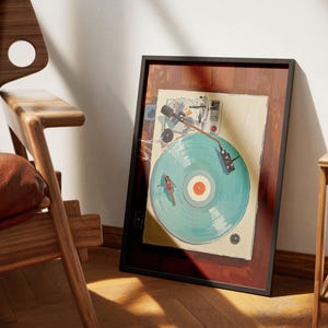 May include: Framed artwork featuring a vintage record player with a turquoise vinyl record. The artwork has a black frame and a brown border. The record has a red center and a painted design of a person surfing. The artwork is leaning against a white wall.