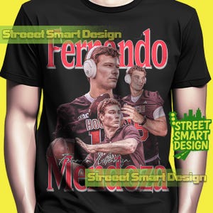 May include: Black t-shirt with a collage of a football player wearing headphones. The design includes the name "Fernando Mendoza" in red, along with the text "Street Smart Design". The player is wearing a maroon jersey.