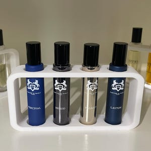 May include: A selection of perfume samples in glass vials with black lids, presented in white holders. The samples are labelled with names such as "Percival", "Herod", "Pegasus", and "Layton". The vials feature a logo and text.