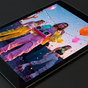 May include: A group of people in colorful outfits, including pink, yellow, and blue, are gathered outdoors. One person holds a pink boombox. Balloons and confetti are in the air. The scene is captured on a tablet.