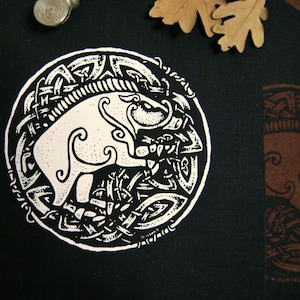 Pode incluir: Remendo de tecido preto com um design de nó celta branco que apresenta um javali estilizado dentro do nó.