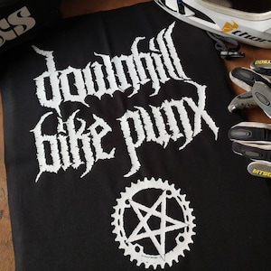 Op de afbeelding: Zwart-witte patch met de tekst "Downhill Bike Punk" in gotische letter. Onder de tekst staat een witte vijfpuntige ster in een wit tandwiel.