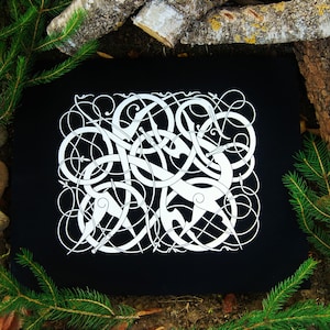 May include: A black fabric square with a white intricate knotwork design. The design is a traditional Scandinavian knotwork pattern.