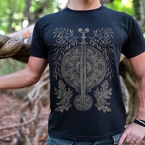 May include: A black t-shirt with a graphic design of a sword and shield surrounded by stylized leaves and berries.