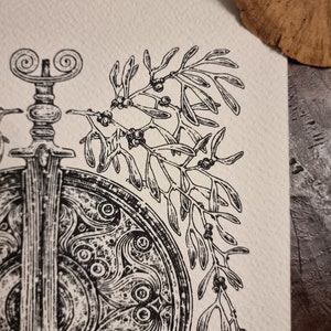 May include: A black and white illustration of a sword and shield with a sprig of mistletoe with berries.