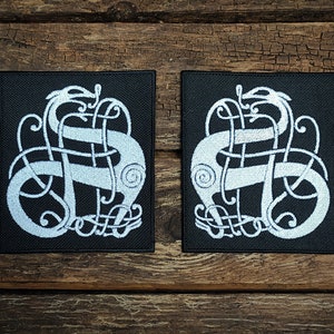 May include: Two black fabric patches with white embroidered designs of a stylised dragon or serpent. The design is a knotwork pattern with a spiral at the top of the dragon's head.