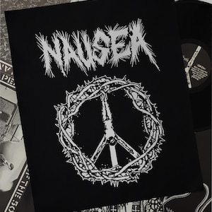 Puede incluir: Parche blanco y negro con la palabra "NAUSEA" en una fuente estilizada y un signo de paz rodeado de espinas.