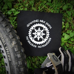 Könnte beinhalten: Schwarzer Patch mit weißem Text, der "downhill bike punx no brakes no masters" lautet, mit einem weißen Zahnrad-Design in der Mitte.