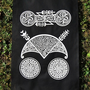 Puede incluir: Tapiz de tela negra con diseños de nudos celtas en blanco. Los diseños incluyen un círculo, una luna creciente y una flecha estilizada.