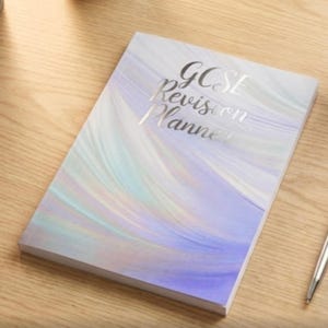 May include: A GCSE Revision Planner with a swirling pastel design in shades of lavender, blue, and white. The title is in silver script. The planner is on a wooden surface.
