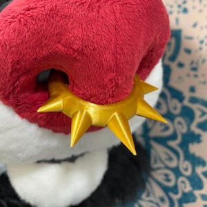 May include: Close-up of a plush red and white animal nose with a gold, spiked ring around the nostril.
