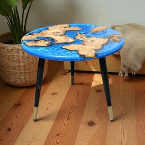 May include: A round side table with a blue epoxy resin top and natural wood inlays. The table has three black legs with gold-colored tips. The table is approximately 20 inches in diameter and 18 inches tall.