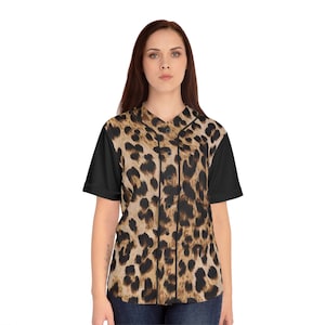 Puede incluir: Una camiseta de béisbol con estampado de leopardo en la parte delantera y el cuello, con mangas cortas negras lisas. La camiseta tiene una parte delantera abotonada y un diseño clásico de camiseta de béisbol.
