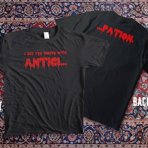 Puede incluir: Camisetas negras con texto rojo. La camiseta delantera dice "I SEE YOU SHIVER WITH ANTICI..." en una fuente goteante. La camiseta trasera dice "...PATION" en la misma fuente. Las camisetas se muestran sobre una alfombra estampada.