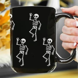 Black ceramic mug with playful white skeletons dancing, designed as a humorous activist and spooky Halloween coffee cup.