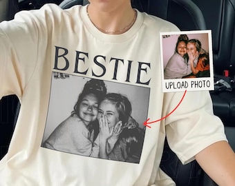 May include: Cream-colored t-shirt with the word "BESTIE" in bold, black letters above a black and white photo of two smiling people. A small photo with the text "UPLOAD PHOTO" is also visible.