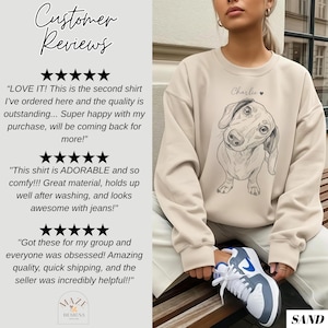 May include: Sand-colored sweatshirt featuring a sketched dachshund dog illustration with the name "Charlie" above it. The sweatshirt is part of a collection, as indicated by the "MAZE DESIGNS" logo. Customer reviews are also visible.