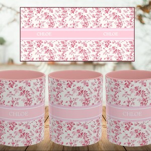 May include: Three ceramic mugs with a floral pattern in pink and white. Each mug has a pink interior and handle. A pink band with the name "CHLOE" is printed on each mug. A matching floral design is in the background.