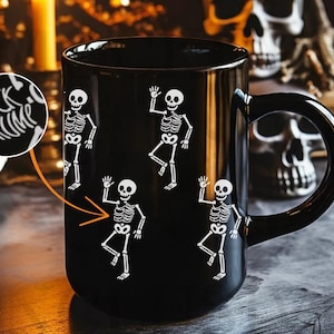 May include: Black ceramic mug featuring white skeleton illustrations in various poses. The mug also has the text "FUCK TRUMP" in a circular design. The mug has a black handle and is likely for Halloween or spooky-themed decor.