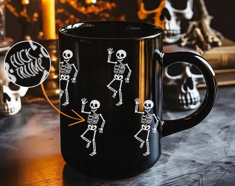 May include: Black ceramic mug featuring white skeleton illustrations in various poses. The mug also has the text "FUCK TRUMP" in a circular design. The mug has a black handle and is likely for Halloween or spooky-themed decor.