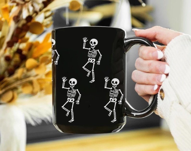 Black ceramic mug with playful white skeletons dancing, designed as a humorous activist and spooky Halloween coffee cup.