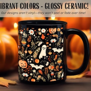 May include: Black ceramic mug with a Halloween-themed floral design. The mug features pumpkins, ghosts, and bats among flowers in orange, white, and beige. Text on the mug reads "VIBRANT COLORS - GLOSSY CERAMIC!" and "Our designs aren't vinyl-they won't peel or fade over time!"