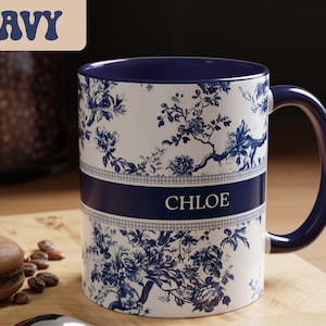 May include: A white ceramic mug with a navy blue handle and interior. The mug features a floral design in navy blue and the name "CHLOE" in white. The word "NAVY" is in a navy blue banner in the upper left corner.
