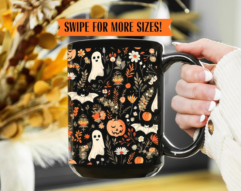 May include: Black ceramic mug with a Halloween-themed floral design. The design includes pumpkins, bats, ghosts, and flowers in orange, white, and black. The mug has a black handle and the text "SWIPE FOR MORE SIZES!" in an orange banner.