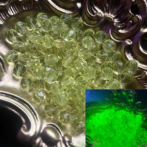 Puede incluir: Un conjunto de cuentas facetadas de color verde claro llena un plato decorativo de color dorado. Las cuentas tienen una cualidad translúcida, captando la luz. Una imagen más pequeña insertada muestra las cuentas brillando en verde brillante.