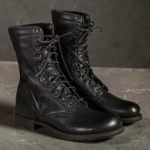 May include: A pair of black leather combat boots featuring a high-top silhouette, rounded toes, and a lace-up front closure with metal eyelets. The boots have a sturdy sole, a reinforced heel, and a textured finish on the leather upper material.