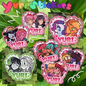 以下が含まれることがあります： 様々なアニメスタイルのキャラクターが描かれた、カラフルなYuriステッカーのコレクション。各ステッカーはハート型で、白いレースの縁取りがあり、下部に「Yuri」の文字が入っています。ステッカーは緑の葉の背景に配置されています。
