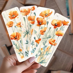 May include: Four rectangular bookmarks featuring watercolor illustrations of orange poppies with green stems and leaves. The bookmarks are held in a hand, with a blurred background of open books.