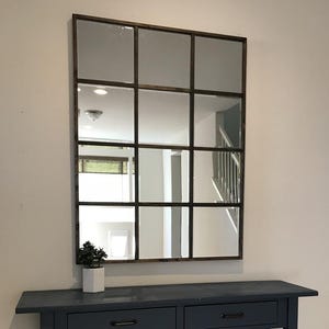 Może przedstawiać: Duże, prostokątne lustro z kratownicą wisi nad granatową konsolą. Rama lustra jest ciemnobrązowa, a stół ma dwie szuflady i półki z listew. Mała roślina doniczkowa stoi na stole.