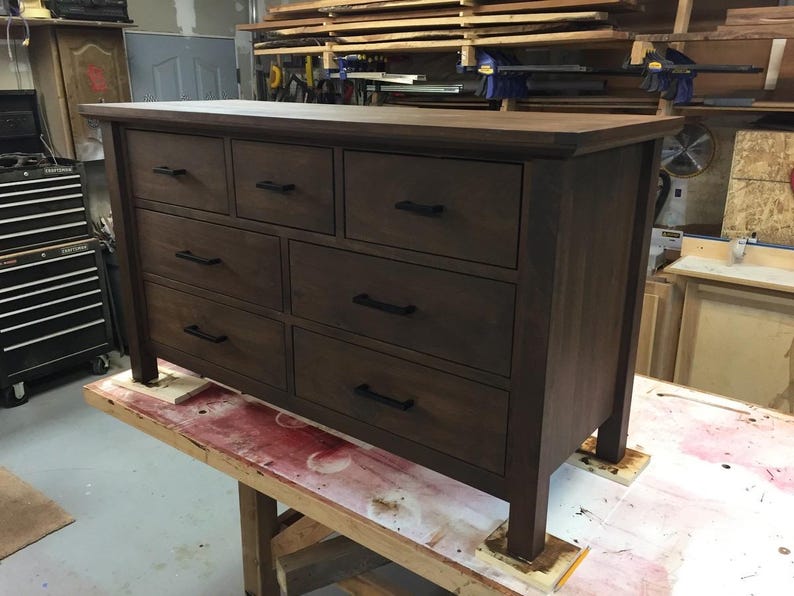 Op de afbeelding: Een donkerbruine houten dressoir met negen laden en zwarte metalen ladegrepen. De dressoir staat op een houten oppervlak.