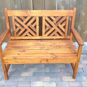 May include: A wooden bench with a slatted seat and a lattice-style back. The bench is stained a rich brown color and has a rustic look.