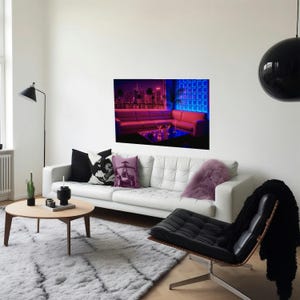 May include: A modern living room with a white sofa, black chair, and a round wooden coffee table. A large framed picture of a neon city scene hangs on the wall. The room has a gray rug and a black hanging light.