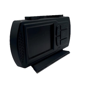 May include: A black rectangular dash camera featuring a front-facing screen, a side panel with a textured honeycomb pattern, and a series of control buttons on the right side. The device is mounted on a flat base and includes top-mounted buttons.