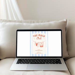 Pu&ograve; includere: Un laptop mostra una grafica per "The Bach Club". Il design presenta un bikini arancione chiaro appeso a un filo stendibiancheria su uno sfondo a strisce blu e bianche. Il laptop &egrave; su un divano color crema.