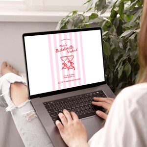 May include: A laptop displaying a pink and white invitation for "Olivia's Bachelorette Weekend." The invitation features two champagne glasses with bows, event details, and a phone number. The laptop is on a person's lap.