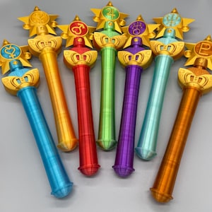 K&ouml;nnte beinhalten: Eine Sammlung von sieben Zauberst&auml;ben mit zylindrischen Griffen in Blau, Orange, Rot, Gr&uuml;n, Violett, T&uuml;rkis und Braun. Jeder Stab ist mit einem goldenen Sternemblem versehen, das ein einzigartiges Planetensymbol in der Griffarbe enth&auml;lt.