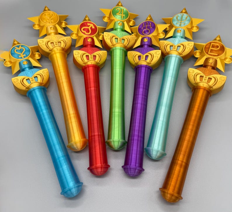 K&ouml;nnte beinhalten: Eine Sammlung von sieben Zauberst&auml;ben mit zylindrischen Griffen in Blau, Orange, Rot, Gr&uuml;n, Violett, T&uuml;rkis und Braun. Jeder Stab ist mit einem goldenen Sternemblem versehen, das ein einzigartiges Planetensymbol in der Griffarbe enth&auml;lt.
