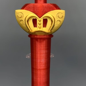 K&ouml;nnte beinhalten: Ein 3D-gedruckter Zauberstab mit einem gelben Stern an der Spitze und einem roten kreisf&ouml;rmigen Zentrum, das ein Mars-Symbol zeigt. Der Stab hat einen roten zylindrischen Griff und einen dekorativen gelb-roten Basisabschnitt mit drei kleinen vertikalen rechteckigen Aussparungen.