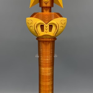 K&ouml;nnte beinhalten: Ein 3D-gedrucktes Zepter mit einem metallisch orangefarbenen zylindrischen Griff und einem gelben sternf&ouml;rmigen Aufsatz. In der Mitte des Sterns befindet sich ein kreisf&ouml;rmiges Emblem mit dem Buchstaben P, erg&auml;nzt durch eine geschwungene gelbe Basis.