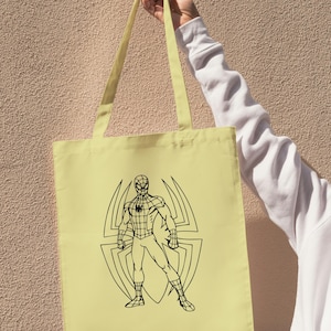 May include: A light yellow tote bag featuring a black outline illustration of Spider-Man standing in front of a spider web design. The bag has matching yellow straps and is held up against a textured wall.