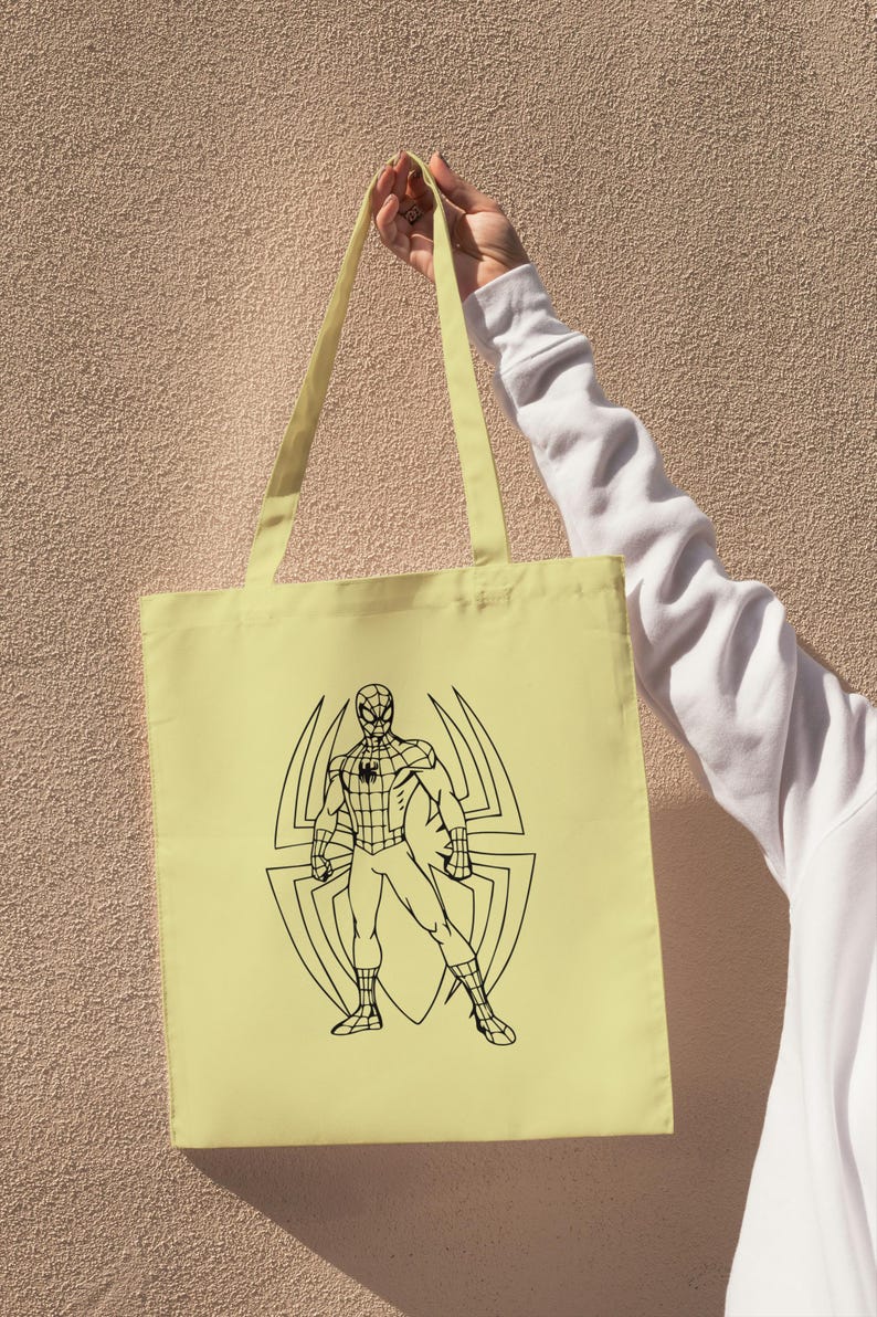 May include: A light yellow tote bag featuring a black outline illustration of Spider-Man standing in front of a spider web design. The bag has matching yellow straps and is held up against a textured wall.
