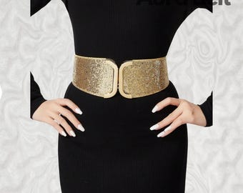 May include: A gold sparkly belt with a large, gold, rectangular buckle. The belt is worn over a black dress.
