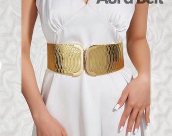 May include: A gold-toned belt with a snakeskin pattern and a double buckle closure. The belt is worn over a white dress. The text "Aura Belt" is visible in the top right corner of the image.