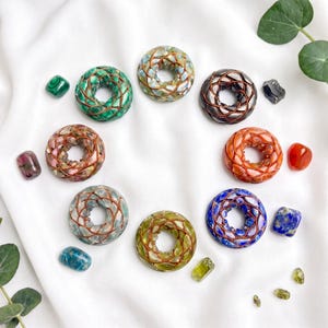 May include: Seven circular donut-shaped pendants made of various colorful gemstones wrapped in thin copper wire. The stones include green, light blue, dark gray, orange, pink, light green, and deep blue, arranged in a circle with loose stones.