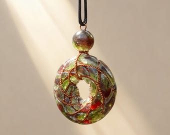 May include: A handmade pendant necklace featuring a circular, donut-shaped pendant. The pendant is crafted from green and red glass pieces, held together with copper wire. A matching bead and black cord complete the necklace.